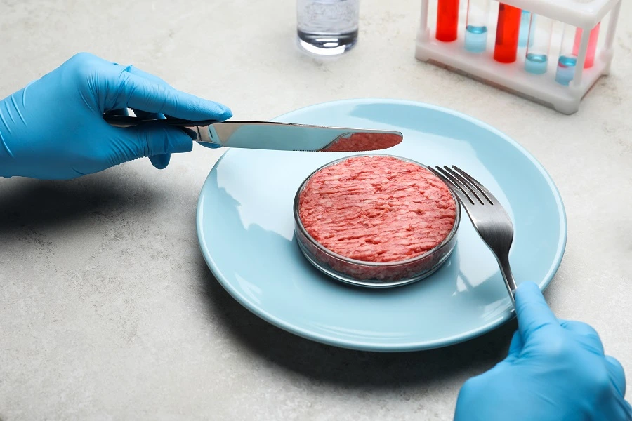 hands in blue gloves holding knife and fork over a blue plate with cell based meat
